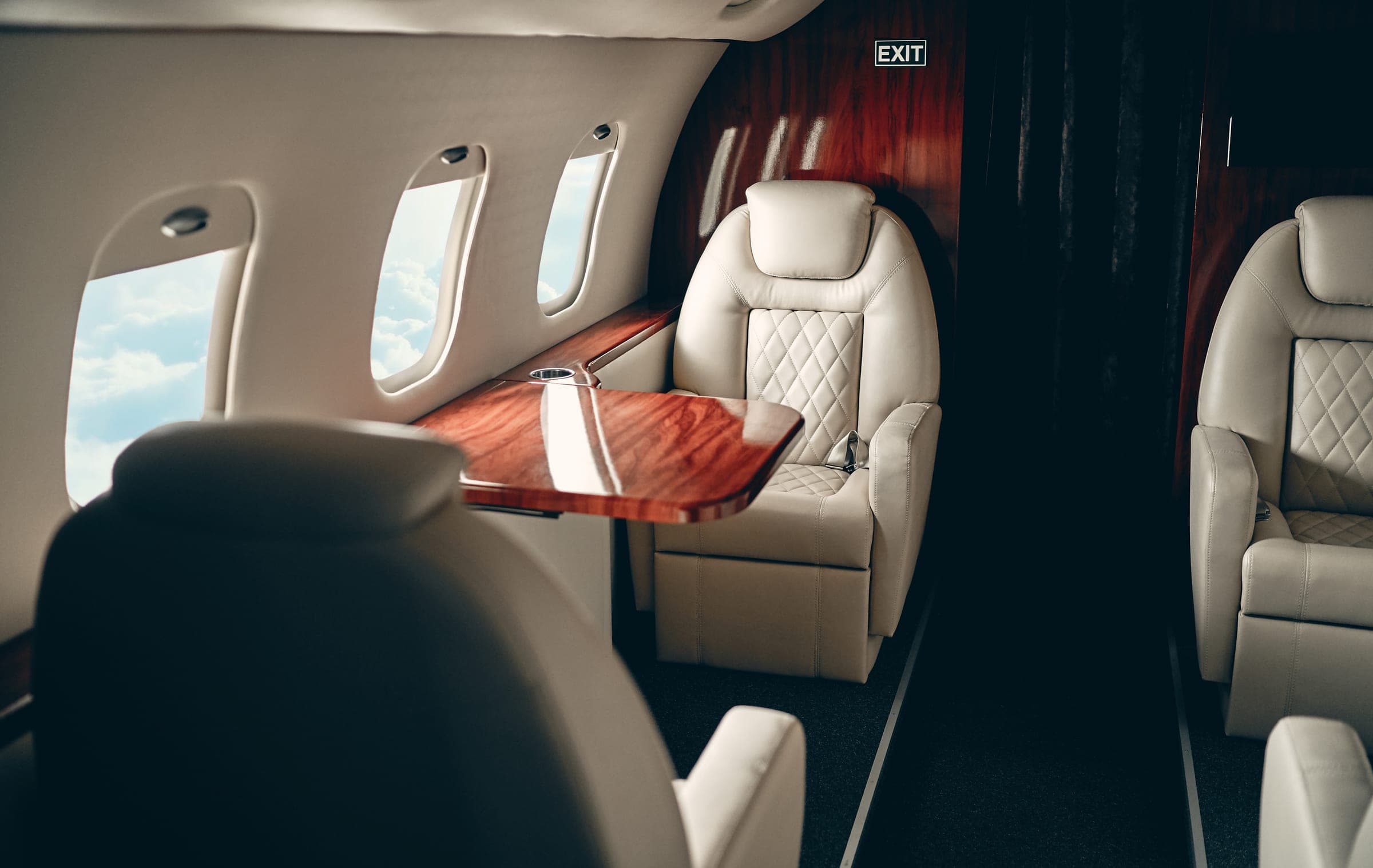 Cream club seats and a wood table in a quiet jet cabin, sky in the windows