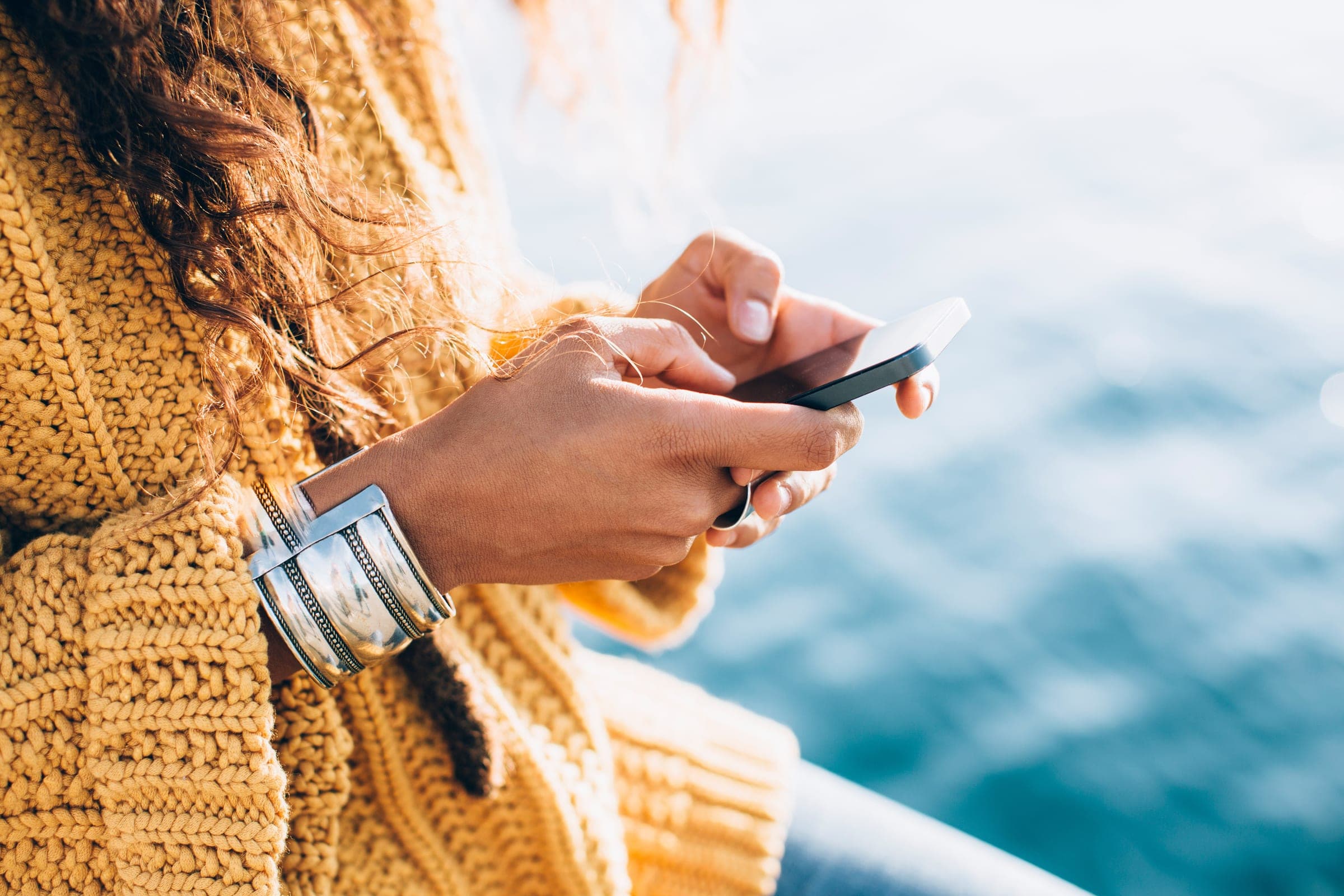 Hands in a knit sweater typing a text, water behind